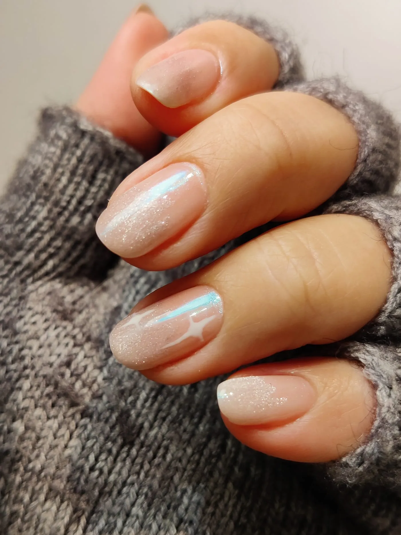 Manicura en tono nude con acabado perlado y detalle de estrellas blancas