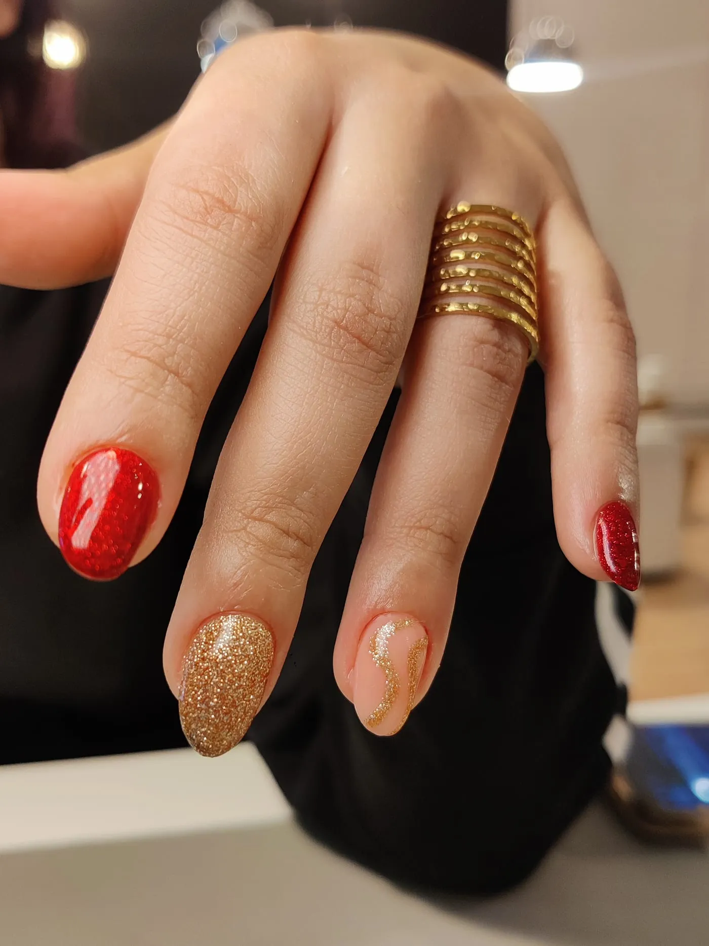 Manicura roja y dorada con purpurina y un trazo ondulado sobre base nude